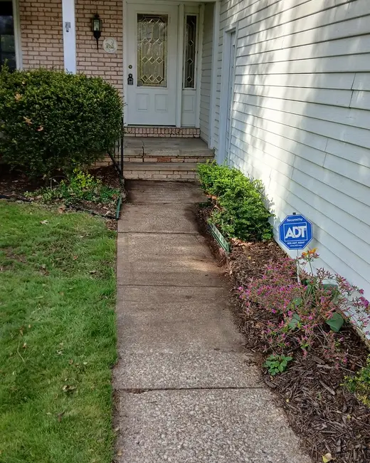 Concrete walkway leading to a house's front door between a lawn and a planting bed