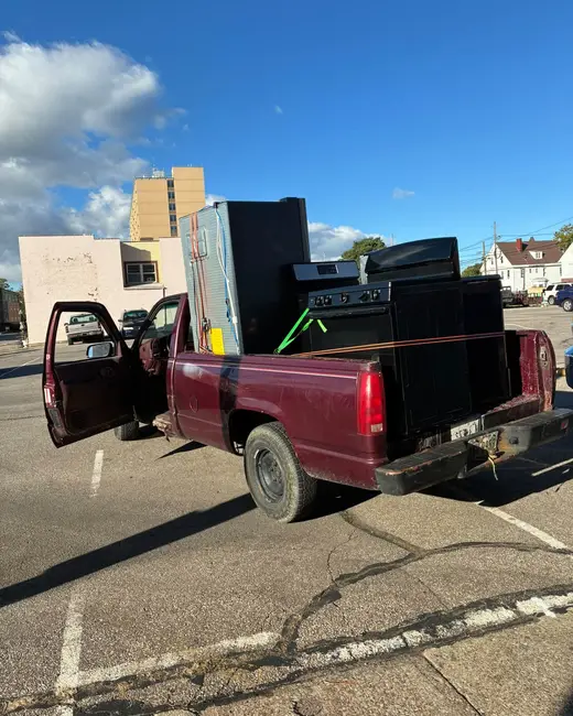 Maroon pickup truck with the tailgate down and household items loaded in the bed