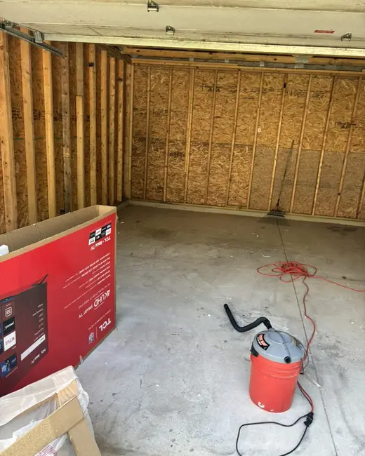 Garage largely emptied, with bare wood walls, a shop vacuum and a few boxes remaining