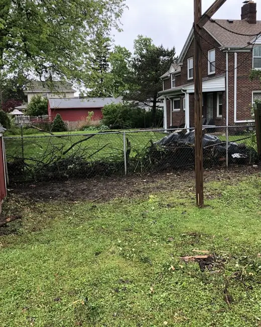Wide view of a grassy back yard with a red shed, a fence and a dolly holding buckets