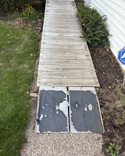Worn wooden walkway with damaged boards running along the side of a house