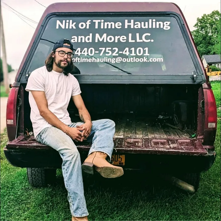 Nik Becker sitting on the tailgate of his maroon pickup, which is lettered with the business name, phone number and email