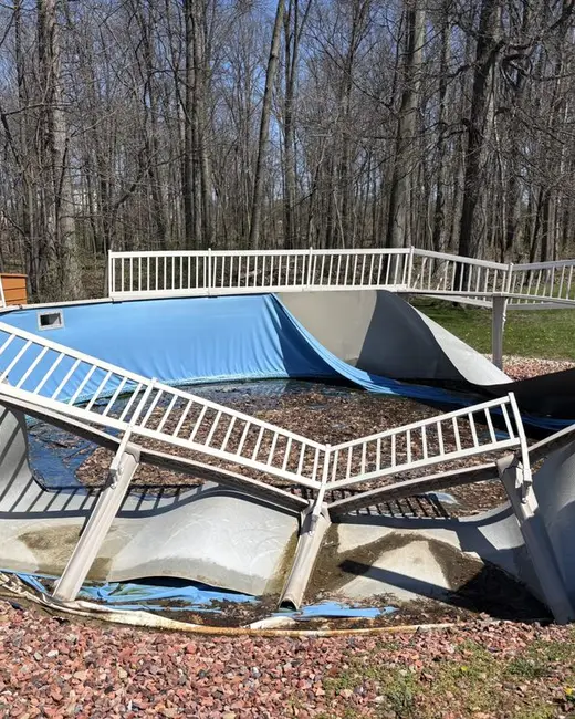 Above-ground pool collapsed and partly dismantled, with bent wall panels and railing on the ground