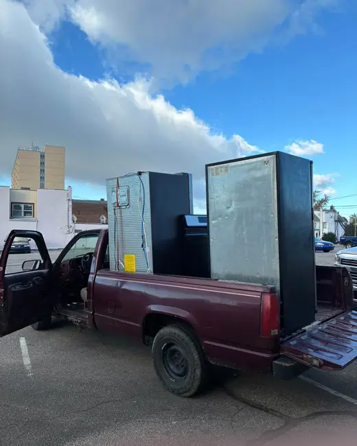 Maroon pickup truck loaded with refrigerators and appliances standing upright in the bed