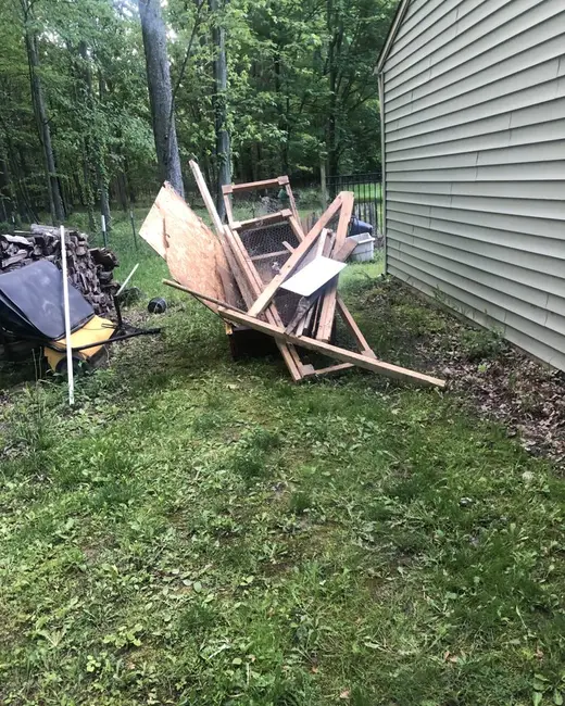Broken furniture and debris piled on the grass beside the siding of a building